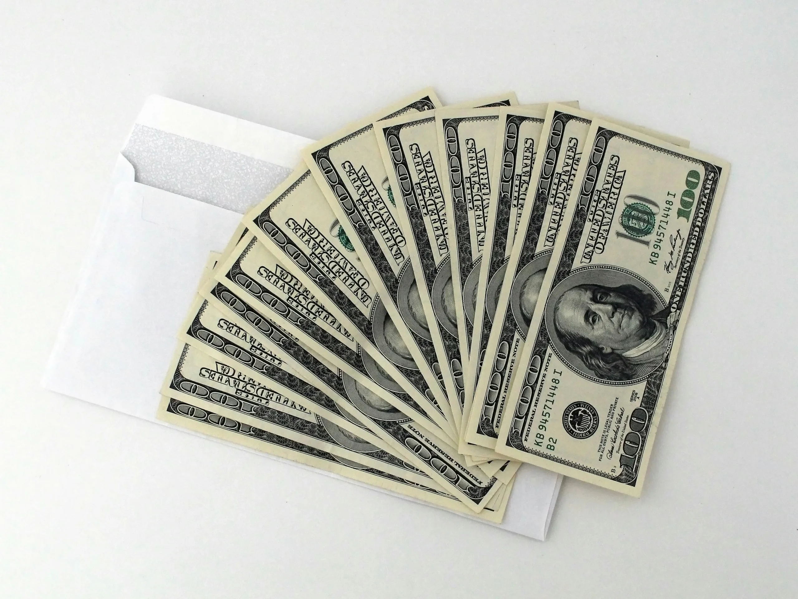 Spread of $100 dollar bills over white envelope on white background