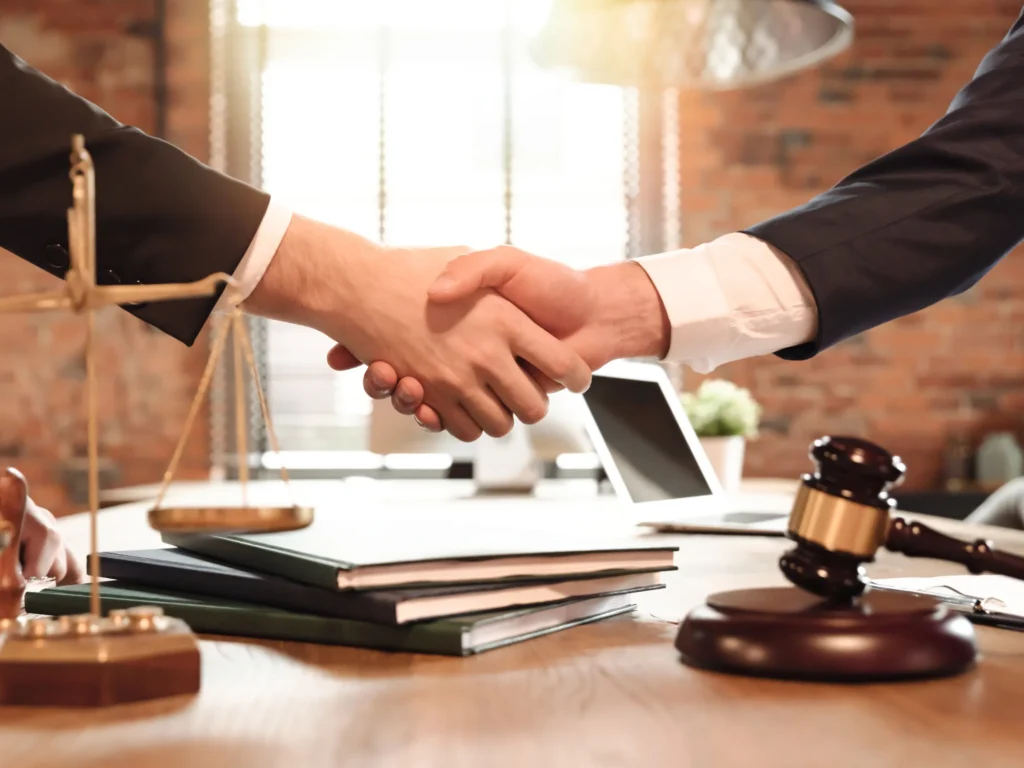 two hands shaking over a desk with books and a gavel on it