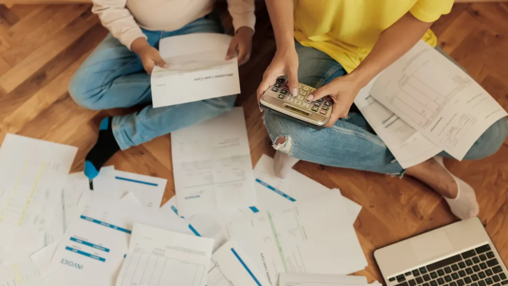 two people sitting on the floor criss-crossed with a lot of papers surrounding them