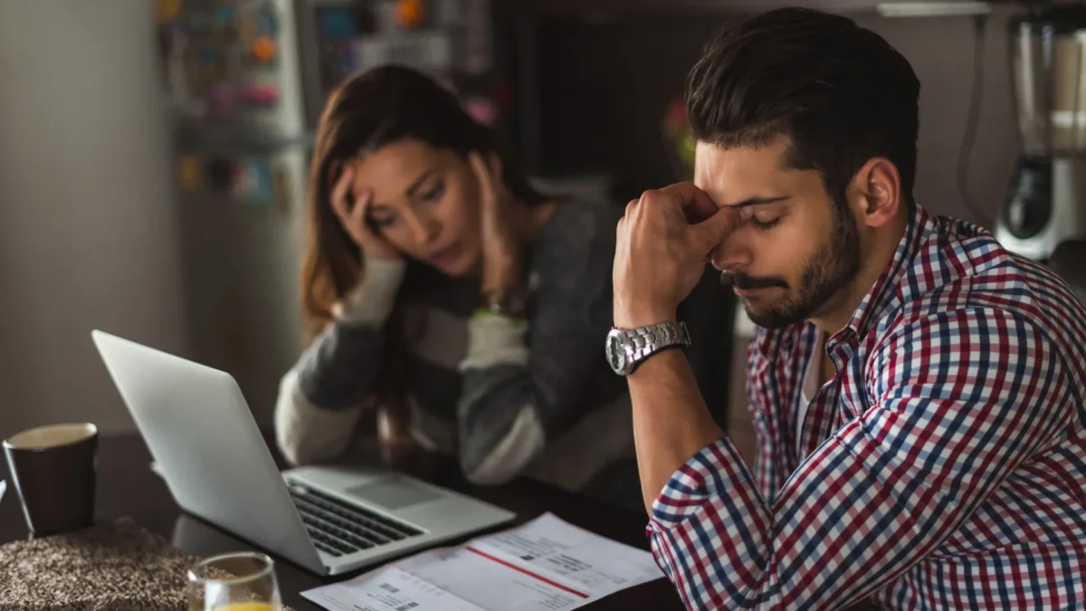 Frustrated and stressed couple sitting at table with laptop and documents because they owe over $50,000 in tax debt