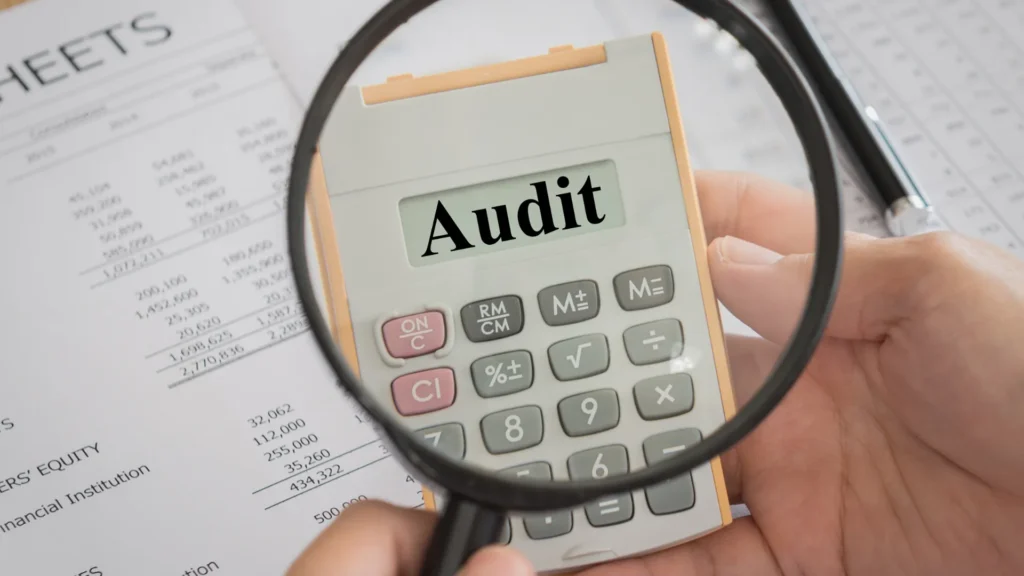 Magnifying glass hovering over calculator with word 'audit' displaying