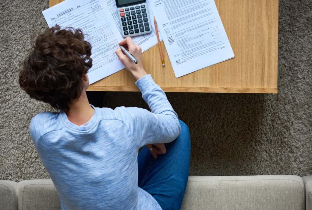 Woman leaning over table with calculator and tax forms