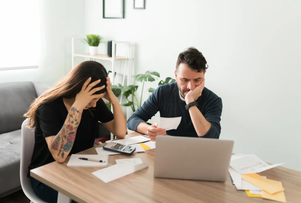 man and woman looking stressed while looking at paperwork and a laptop at a desk