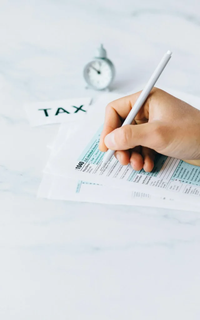 person holding pen and signing tax documents on a white table