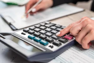 Year-End Tax Tips for 2025: Woman making calculations on a calculator in the foreground, while holding a pen over a clipboard in the background